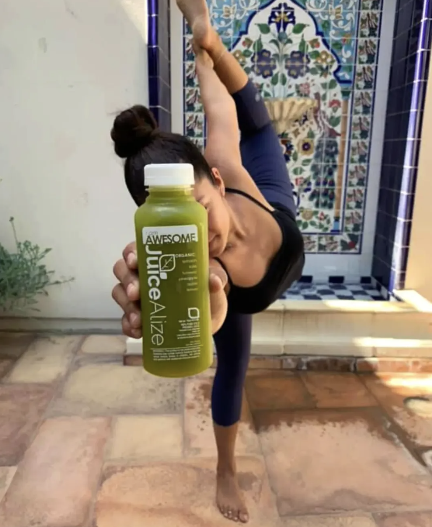 A woman holding up a JuiceAlize I Am Awesome green juice bottle in a yoga pose at a studio pop-up